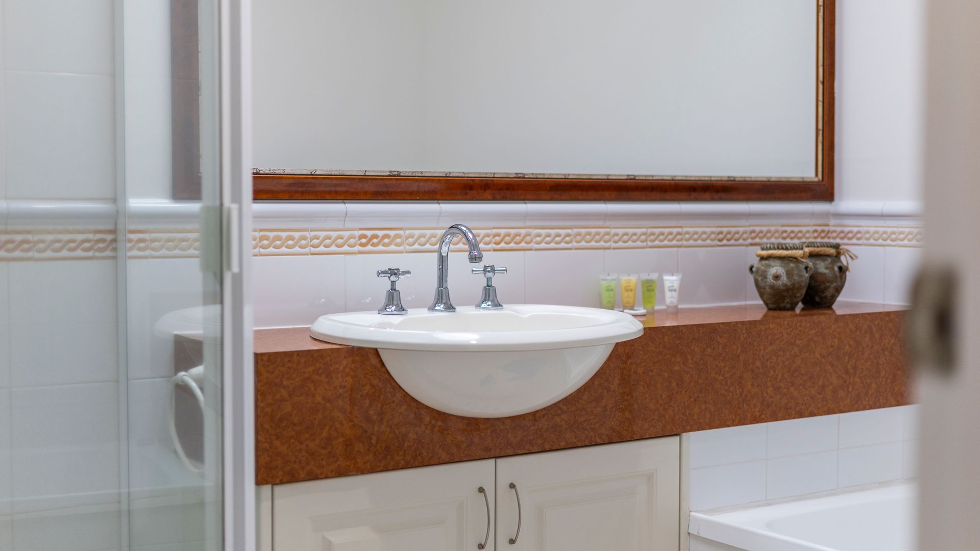 Un bagno con un lavandino bianco, due rubinetti e un piano d'appoggio marrone. Sul mobile ci sono tre prodotti da bagno.