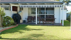 A covered patio with a table and chairs, a barbecue grill, and a garden with plants.