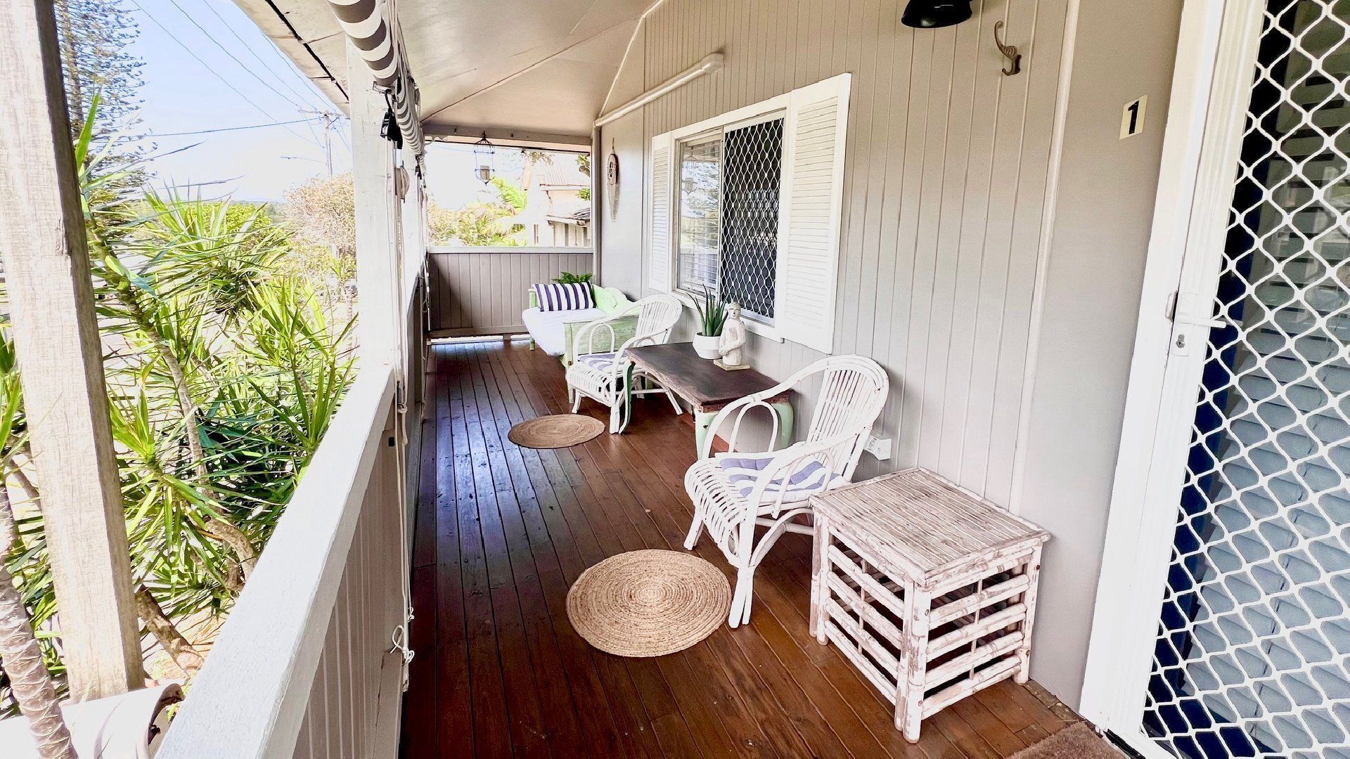 A covered porch with wooden flooring, white wicker furniture, and a small table.