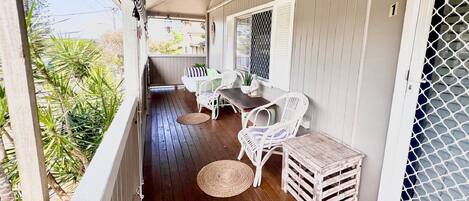 A covered porch with wooden flooring, white wicker furniture, and a small table.