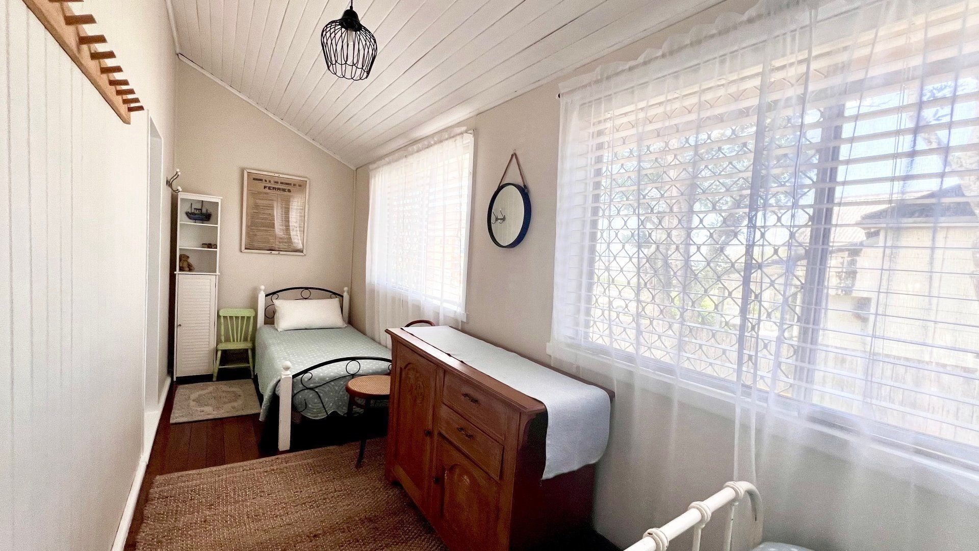 A bedroom with a bed, dresser, and a window with blinds.