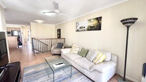 A living room with a white sofa, a glass coffee table, a painting on the wall, and a floor lamp.