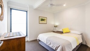 A hotel room with a bed, a desk with a magazine, a lamp, and a painting on the wall.