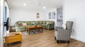 A living room with a green sofa, a grey armchair, a wooden coffee table, and a TV mounted on the wall.