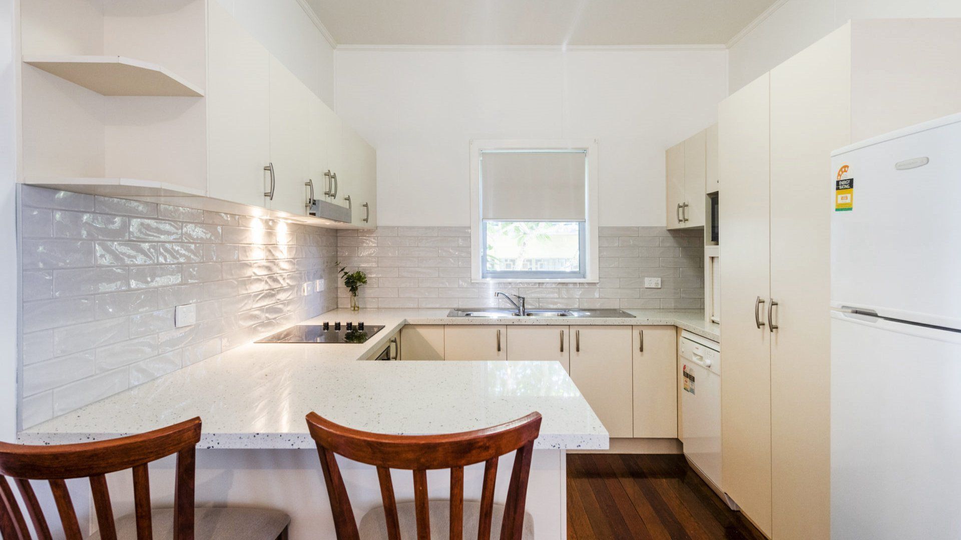A compact kitchen with a central island, a window above the sink, and wooden chairs.