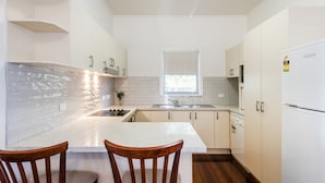 A compact kitchen with a central island, a window above the sink, and wooden chairs. - Brackley Hatch - Lifestyle Yamba (YAMBA)