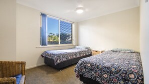 Una camera da letto con due letti singoli, una finestra vista e una sedia in vimini.