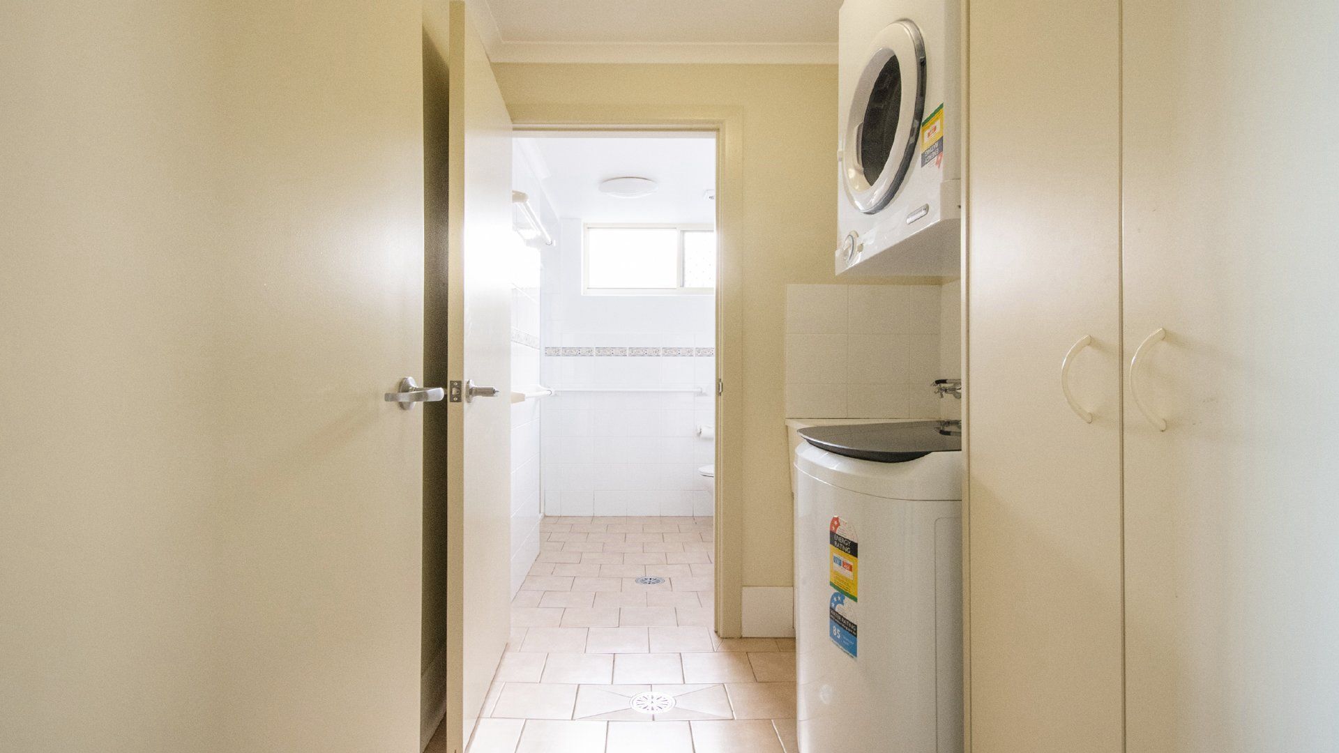 Un couloir étroit avec une porte donnant sur une salle de bain et un espace buanderie équipé d’un lave-linge et d’un sèche-linge.