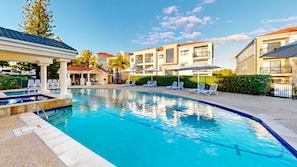 Una piscina con sillas de descanso y sombrillas, rodeada de edificios con balcones.