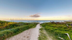 Een kustpad dat naar de zee leidt, met grasvelden en een heldere lucht.