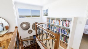 A room with a wooden staircase, a bookshelf filled with books, and a view of the outdoors through a window.