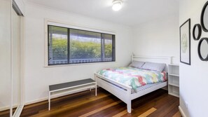 A bedroom with a bed, a bench, a window with blinds, and a wall with framed pictures.