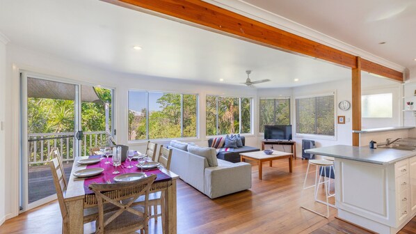 A spacious living area with a dining table set for four, a sofa, a television, and a kitchen area with a bar.