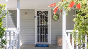 A house with a white door, a welcome mat, and a wreath on the wall.