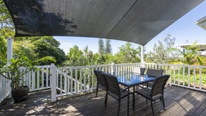 An outdoor deck with a table and chairs, surrounded by a white fence and lush greenery.