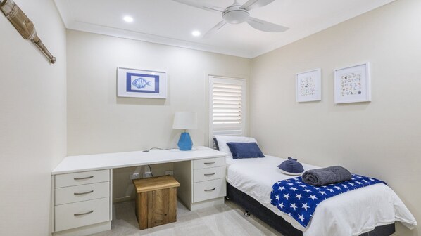 A bedroom with a bed, a desk, a chair, a ceiling fan, and wall art. - Marina Views - Lifestyle Yamba (YAMBA)