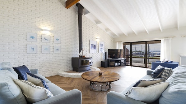 A living room with a white brick wall, a wood-burning stove, a TV, and a view of the marina.