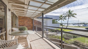 A balcony with a glass table and wicker chairs, overlooking a marina with boats and palm trees.