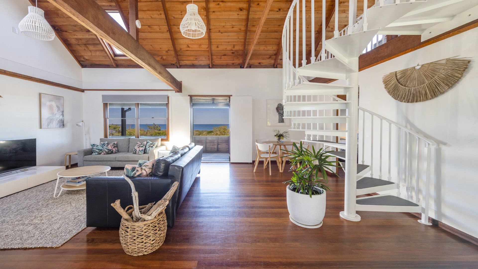 A spacious living room with a wooden staircase, a large window with a view, and a modern interior design.