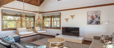 A spacious living room with a large sofa, hanging chairs, a flat-screen TV, and a fireplace.