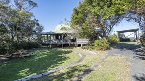 A rustic cabin with a covered porch, a picnic table, and a paved driveway leading to a covered parking area.