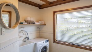 A bathroom with a washing machine, a sink, a mirror, and a window with blinds. - The Point - Lifestyle Yamba (ANGOURIE)