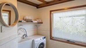 A bathroom with a washing machine, a sink, a mirror, and a window with blinds.