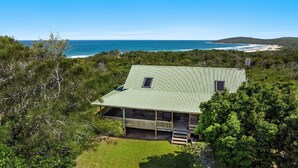 A coastal house with a green metal roof, surrounded by dense greenery and overlooking the ocean. - The Point - Lifestyle Yamba (ANGOURIE)