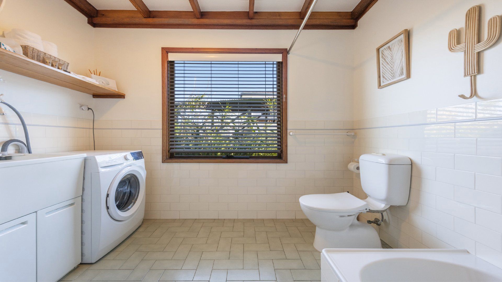 A compact bathroom with a washing machine, toilet, and a window with blinds.