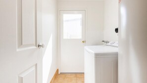 A narrow hallway leading to a door with a window, a white sink, and a tiled floor. - Meridian 9 - Lifestyle Yamba (YAMBA)