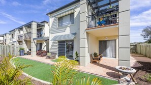 A residential building with multiple balconies, a patio area with outdoor furniture, and a well-maintained lawn. - Meridian 9 - Lifestyle Yamba (YAMBA)