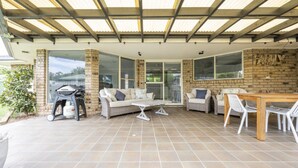 A covered patio area with a barbecue grill, seating arrangements, and a brick wall with the word 'FAMILY' visible. - Yamba Family Seascape - Lifestyle Yamba (YAMBA)