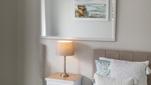 A bedside table with a lamp, a bed with a headboard, and a framed picture on the wall. - Yamba Family Seascape - Lifestyle Yamba (YAMBA)