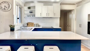 Une cuisine moderne avec des meubles blancs, un mur d’accent bleu, un grand îlot central doté de tabourets et une horloge au mur.