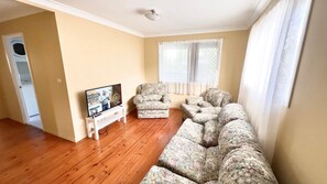 A living room with a sofa set, a television on a stand, and a window with curtains.