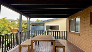 A covered outdoor area with a wooden table and benches, a brick wall, and a view of a house and greenery. - The Perch - Lifestyle Yamba (YAMBA)