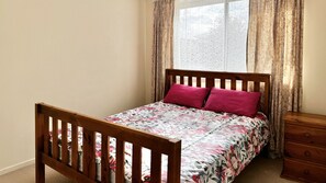 A single bed with a wooden frame, a floral bedspread, and two red pillows.