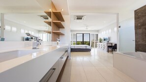 Experience a spacious room with a large bed, sleek bathroom, and modern kitchen area, offering a view of the outdoors.