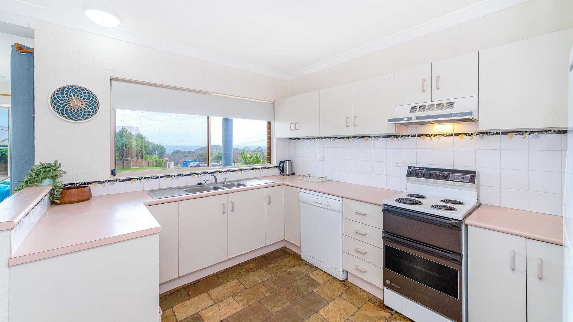 A kitchen with white cabinets, a stove, a sink, and a window with a view.