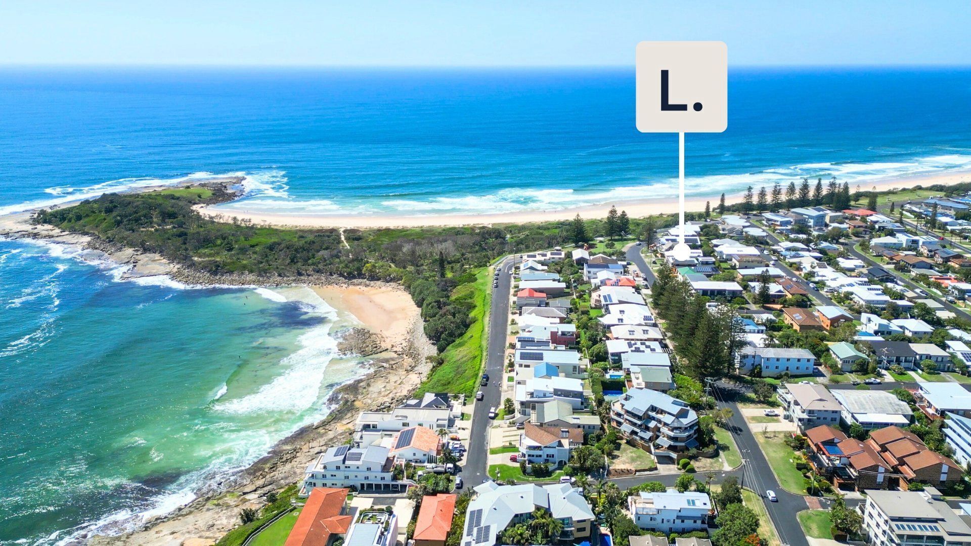 An aerial view of a coastal residential area with houses, a beach, and the ocean.