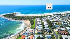 An aerial view of a coastal residential area with houses, a beach, and the ocean.