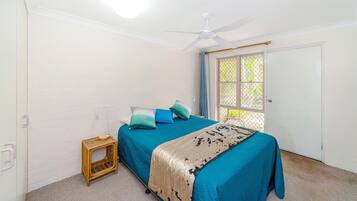 A bedroom with a bed, a ceiling fan, a small table, and a window with a view.