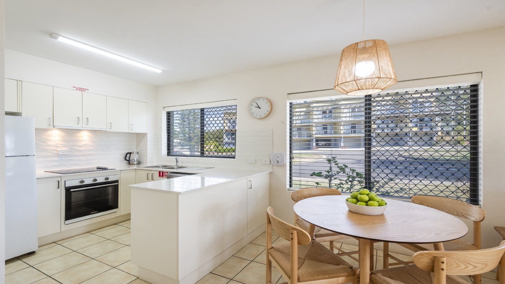 A modern kitchen with white cabinets, a built-in oven, and a dining area with a round table and chairs.