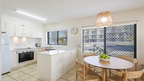 A modern kitchen with white cabinets, a built-in oven, and a dining area with a round table and chairs.