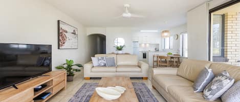 Ein modernes Wohnzimmer mit Flachbildfernseher, zwei Sofas, einem Couchtisch und einer Küche im Hintergrund.