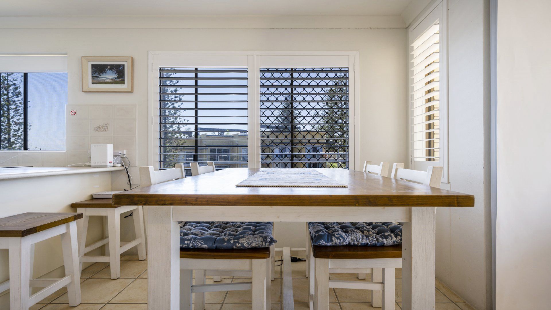 A dining area with a wooden table and white chairs, a window with blinds, and a view of the outside.
