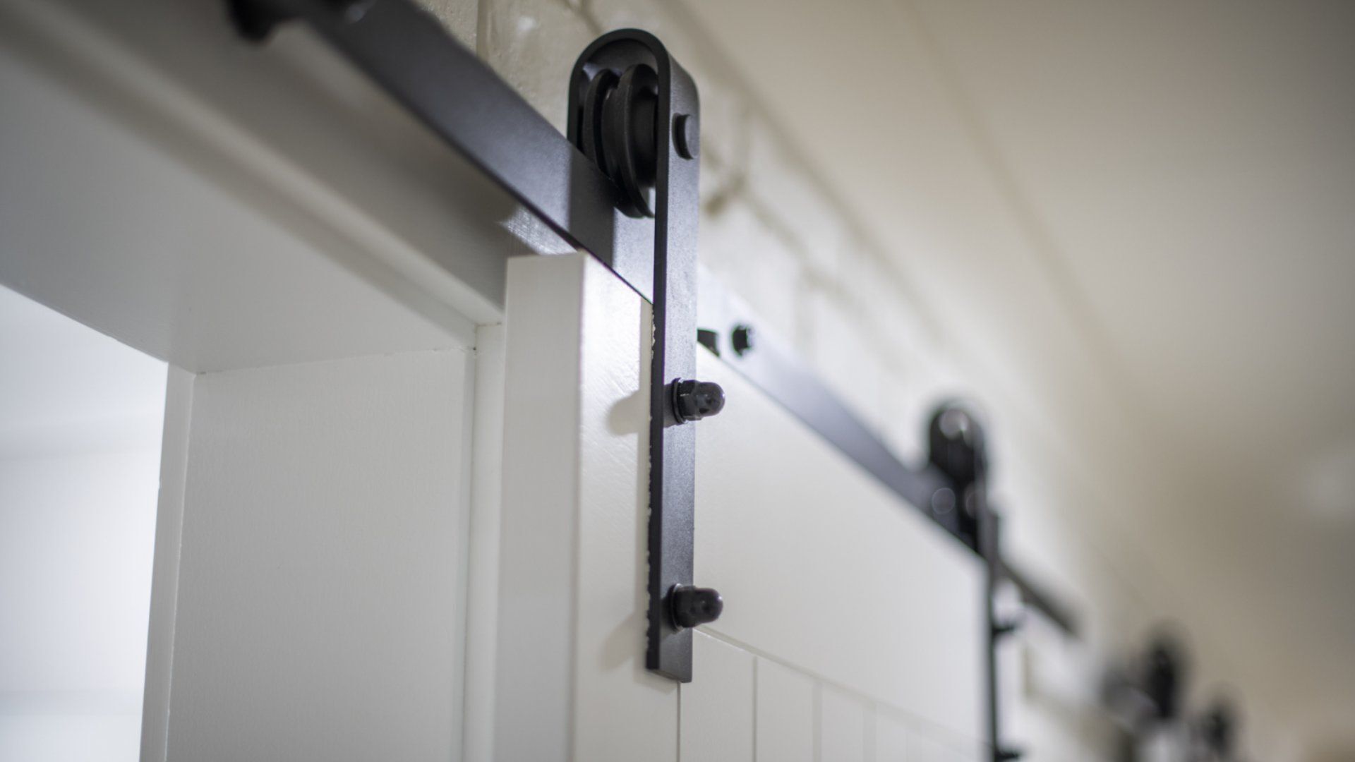 A close-up of a sliding barn door mechanism with a metal track and a black handle.