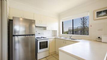 A modern kitchen with stainless steel appliances, white cabinetry, a large window, and a view of buildings outside.