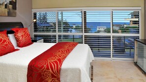 Habitación de hotel con cama, mesita de noche, ventana con persianas y vista al mar.