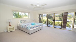 Relax in a serene bedroom with a large bed and ceiling fan, offering a view of the outdoors.